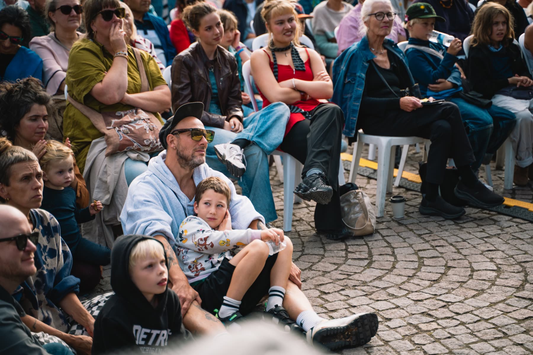 Publikum siddende på brosten
